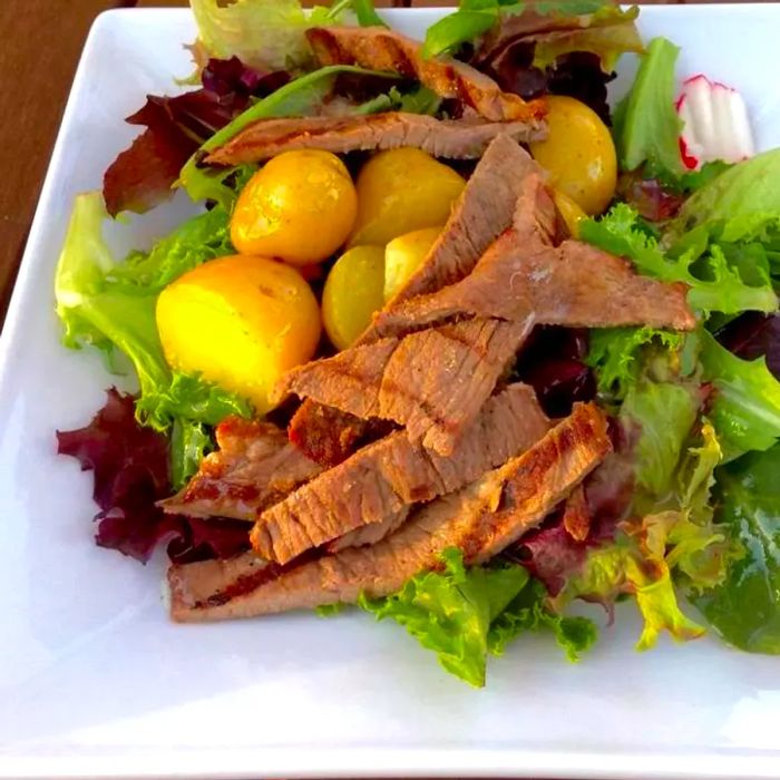 A warm steak and potato salad served on a crisp white plate