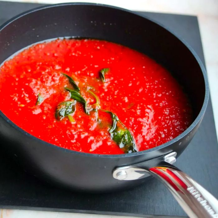 A saucepan filled with vibrant red tomato sauce, topped with a sprig of fresh basil