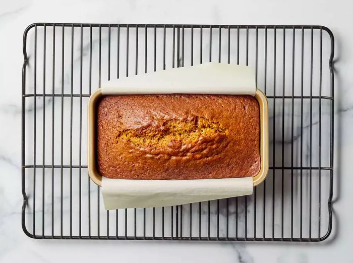 Pumpkin bread cooling in its loaf pan on a wire rack.