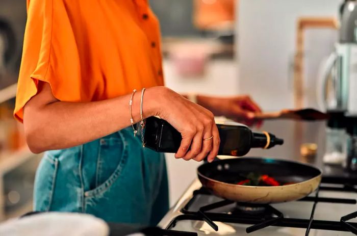 A woman cooking with oil on a gas stove