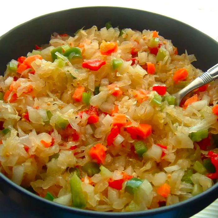 A bowl of sauerkraut with hints of yellow, featuring pieces of carrot and green bell pepper mixed in