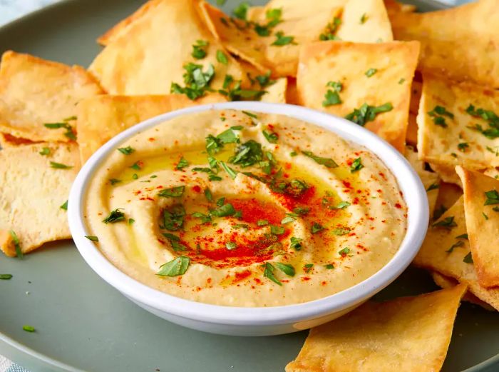 A close-up of a bowl of hummus surrounded by pita chips