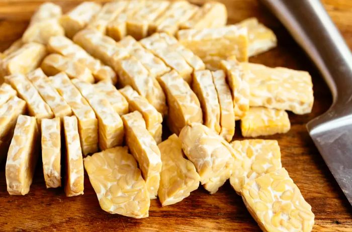 Slices of tempeh on a cutting board with a knife beside it