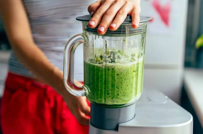 A close-up view of blending a green evening smoothie in a blender bowl.