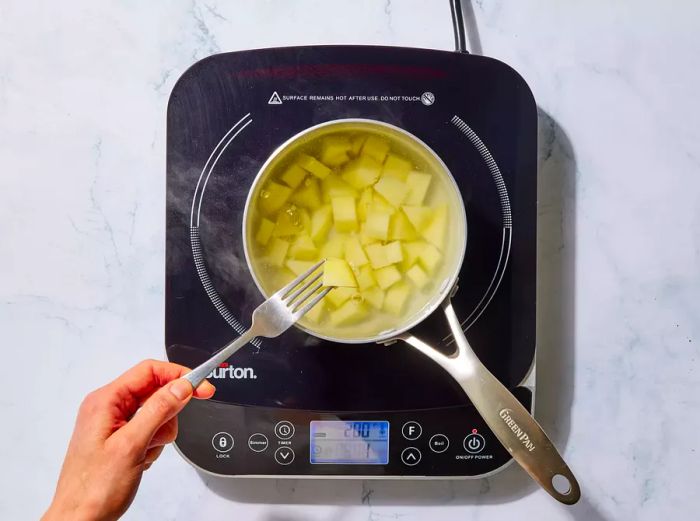 A small pot with cubed potatoes boiling in water.