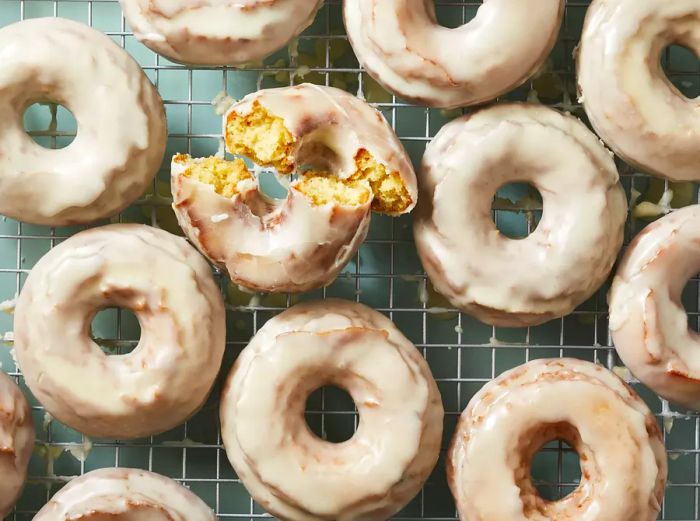 A close-up of sour cream donuts on a wire rack, with one split in half, showing its delicious interior.