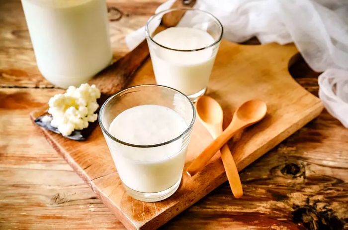 A rustic scene featuring organic probiotic milk kefir grains, Tibetan mushrooms, and kefir grains resting on a wooden spoon, next to a glass of kefir, all placed on a wooden table.