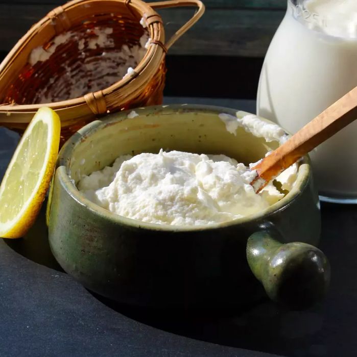 Homemade ricotta in a handled bowl, stirred with a wooden spoon