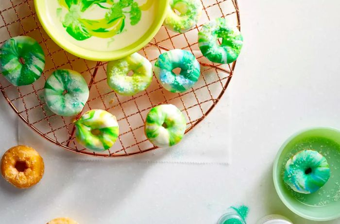 mini doughnuts dipped in a creamy white frosting swirled with vibrant yellow, blue, and green colors