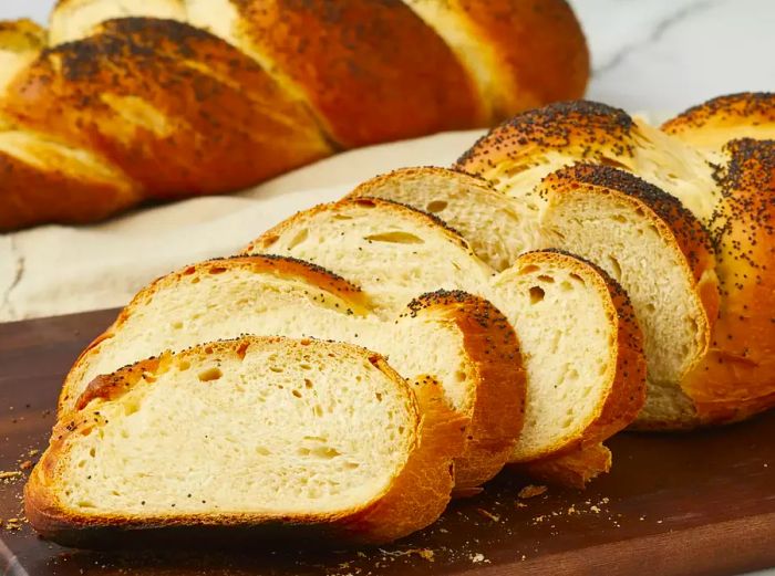 A close-up of Challah bread slices laid on a wooden cutting board, with an entire loaf in the background.