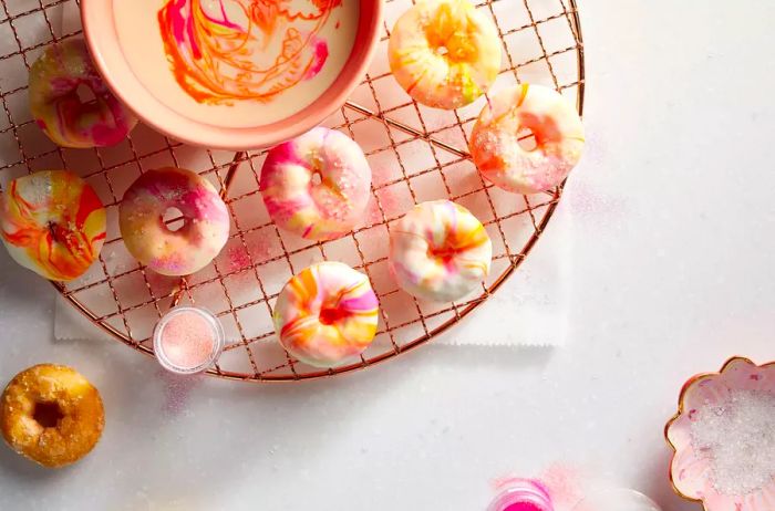 mini doughnuts dipped in a swirl of white frosting with vibrant yellow, pink, and orange hues