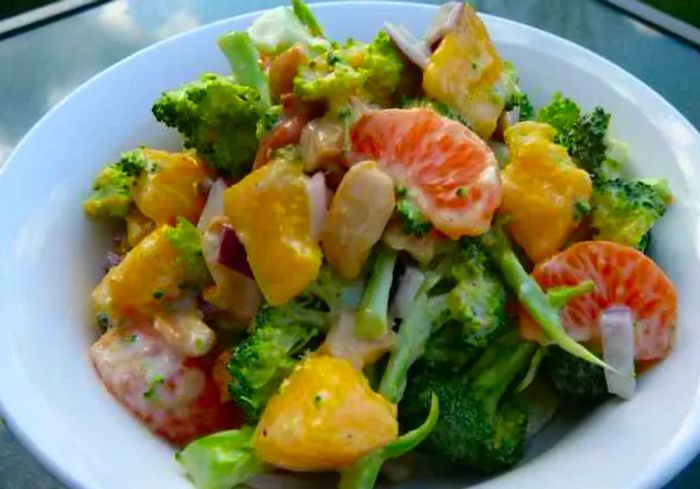 A bowl of broccoli florets, mango chunks, and orange slices.