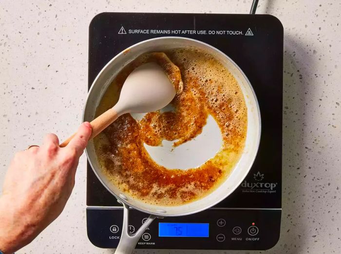 A large pan with brown sugar being mixed into melted butter