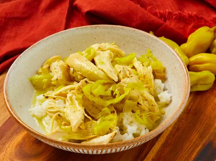 A slight high-angle view of chicken, rice, and pepperoncini peppers served in a beige bowl.