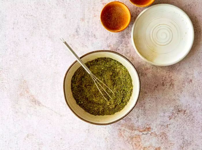 A bowl filled with dried herbs and a small whisk.