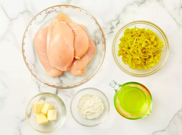 An overhead shot showcasing all the ingredients for Mississippi chicken, neatly arranged in small glass bowls on a sleek marble countertop.