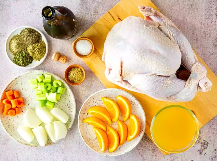 Chopped vegetables, seasonings, sliced citrus, and an uncooked turkey resting on a stone surface.