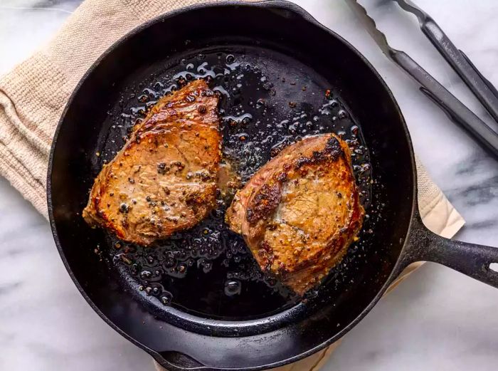 An overhead shot of two steaks, beautifully seared, in a cast-iron skillet.