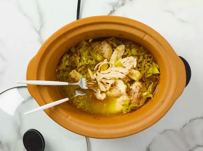 A top-down view of Mississippi chicken being shredded with two forks.