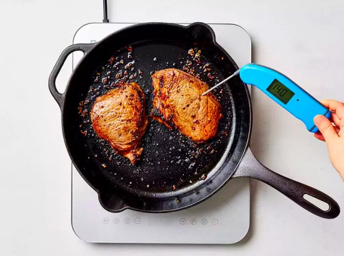 Checking the internal temperature of a steak using a meat thermometer while it's in the skillet.