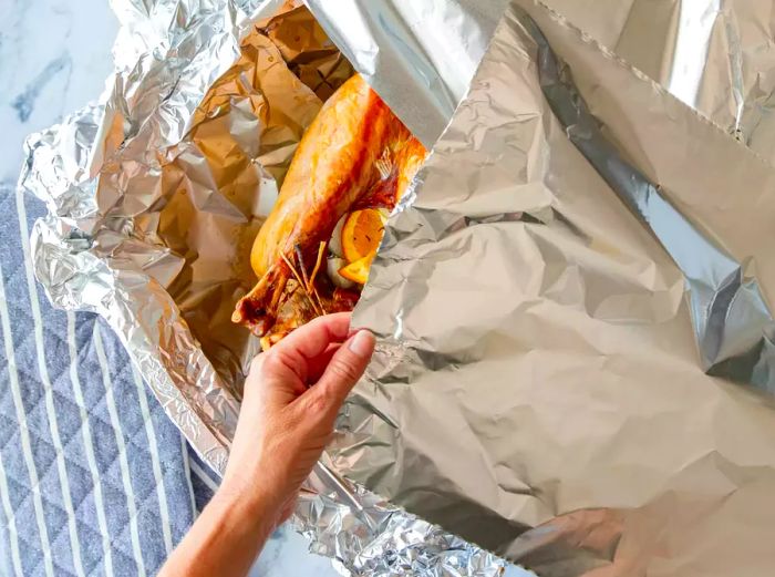 A person removing the foil from a roasted turkey.