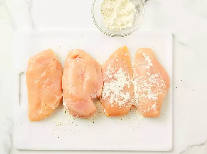 An overhead view of four chicken breasts topped with a dusting of ranch seasoning.