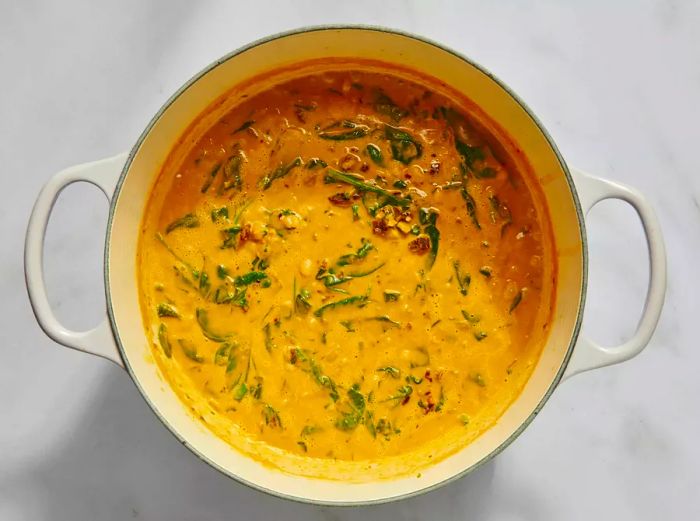 A large Dutch oven filled with Marry Me Bean Soup, topped with basil and spinach