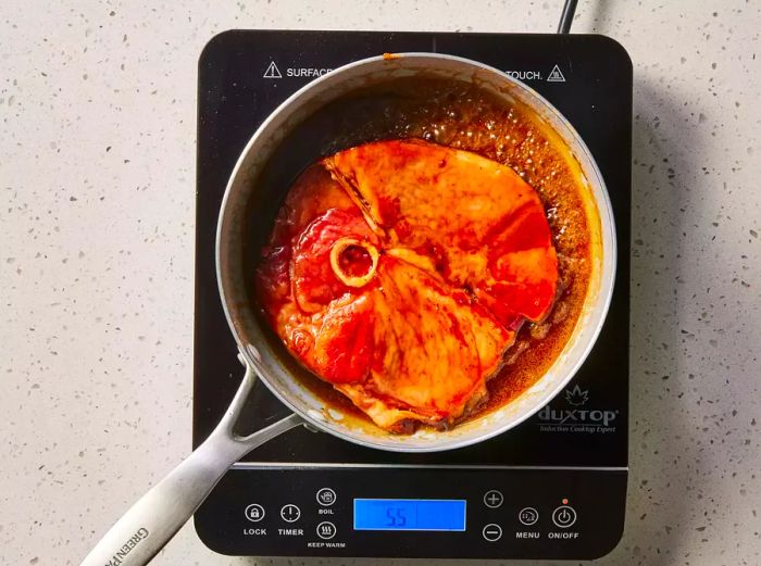 A ham steak simmering in a pan with brown sugar butter glaze