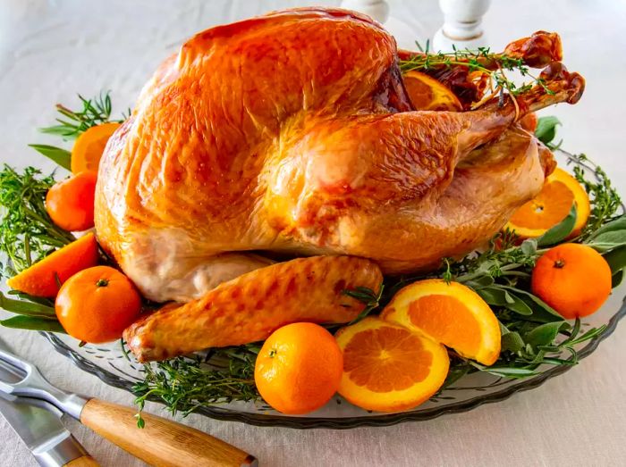 A beautifully roasted turkey displayed on a platter, adorned with fresh herbs and slices of orange.