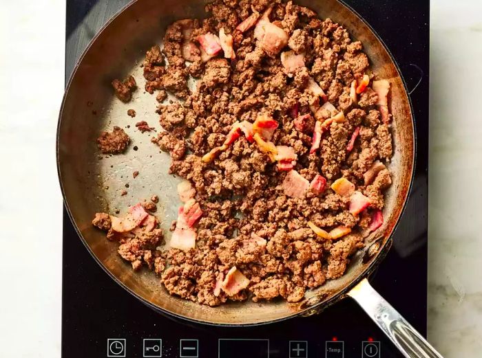 A skillet filled with browned ground beef and chopped bacon