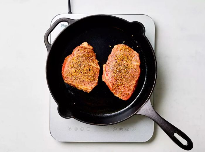 Seasoned steaks sizzling in a cast-iron skillet on the stove.