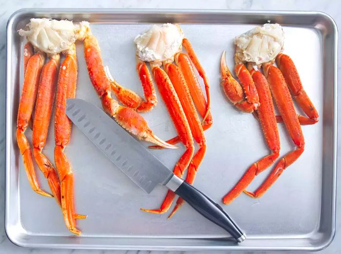 A top-down view of a baking sheet with crab legs being sliced with a knife