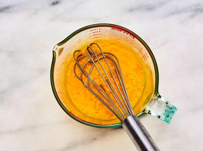 A glass measuring cup filled with whisked eggs, mirin, sugar, soy sauce, and dashi stock