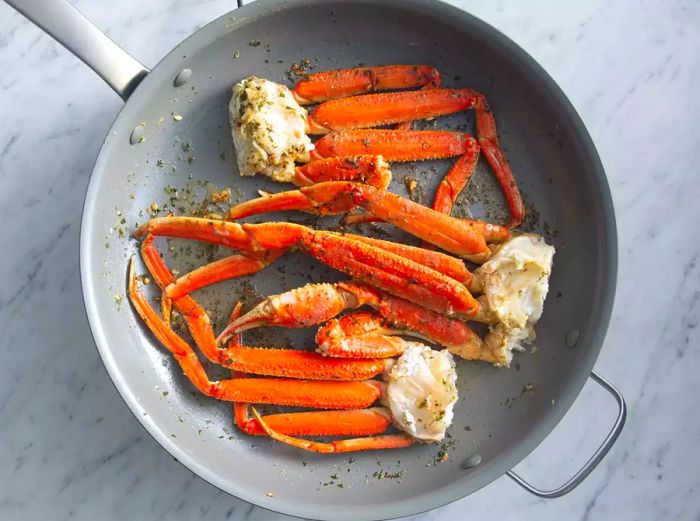 Crab legs in a skillet with garlic and butter, viewed from above