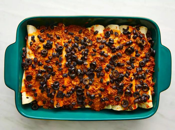 An overhead shot of freshly baked beef enchiladas in a turquoise 9x13 casserole dish.