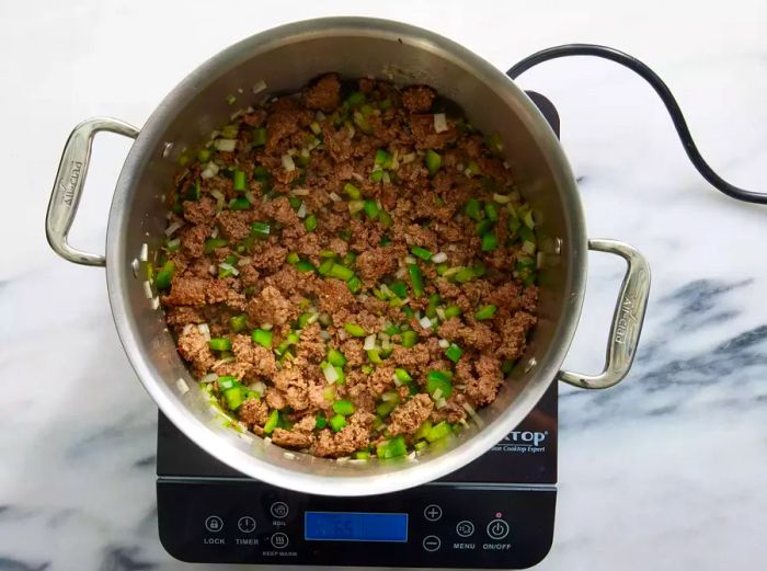 A large pot with cooked ground beef, diced celery, onion, and bell pepper