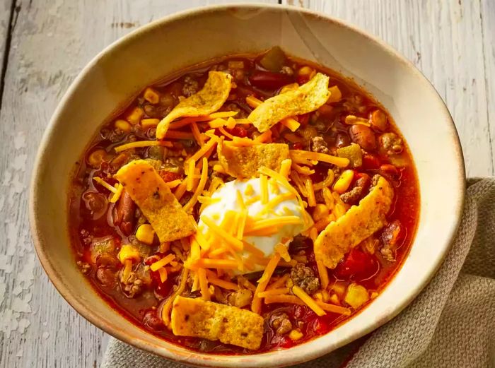 A top-down view of a bowl of taco soup made in the slow cooker, garnished with sour cream, shredded cheddar cheese, and a sprinkle of Frito's chips.