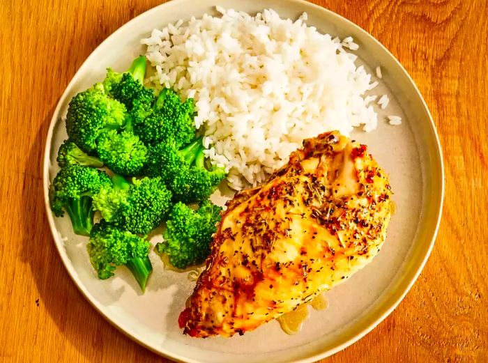 Completed baked split chicken breast served with a side of broccoli and rice.