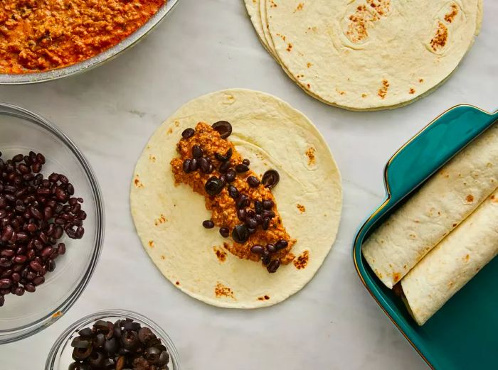 An overhead view of beef enchiladas being rolled and placed into a prepared baking dish.