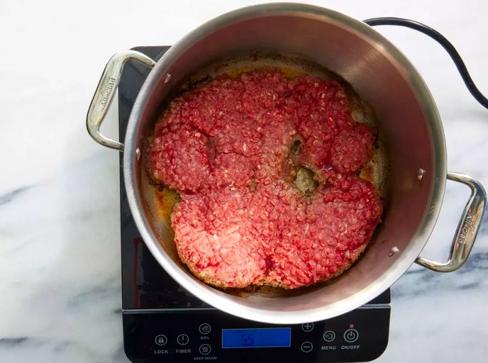 A large ground beef patty sizzling in a pot