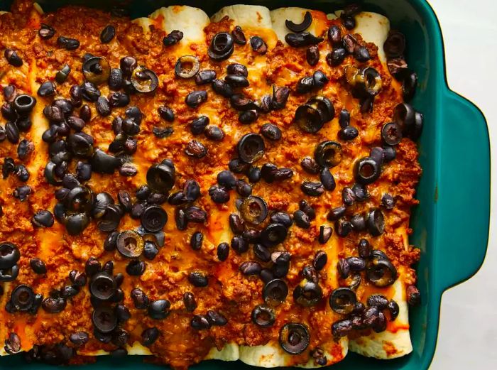 A close-up view of baked beef enchiladas in a turquoise 9x13 casserole dish.