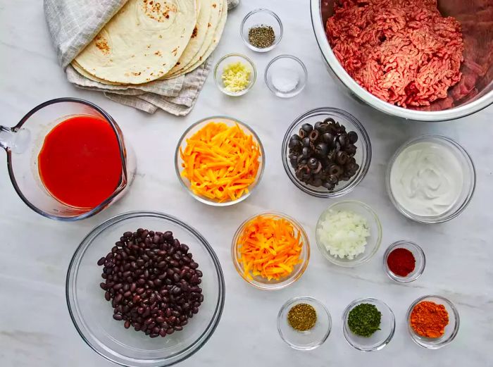 A bird's-eye view of all the ingredients arranged for beef enchiladas, displayed neatly on a marble countertop.