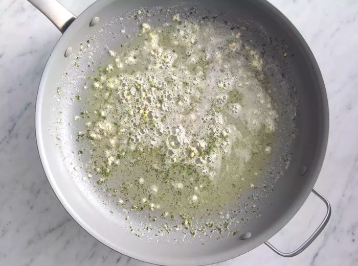 A top-down view of a skillet with melted butter and garlic cooking together