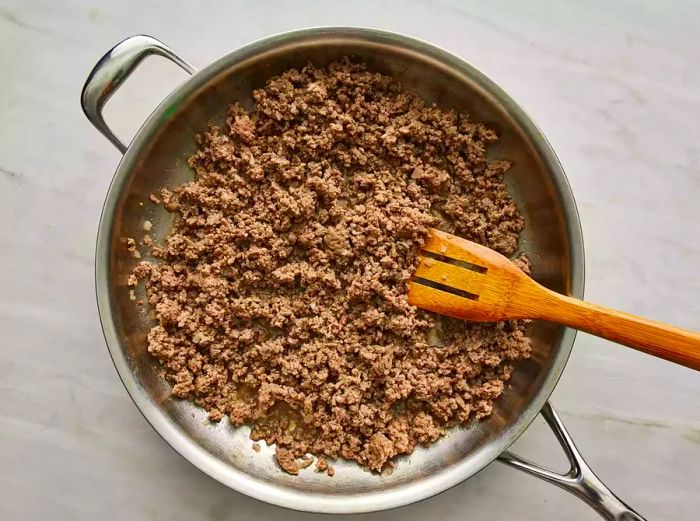 An overhead shot of ground beef and onions being sautéed in a large skillet.