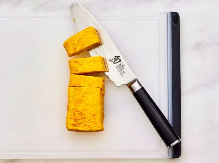 A rolled Japanese tamago omelet on a cutting board, being sliced into pieces