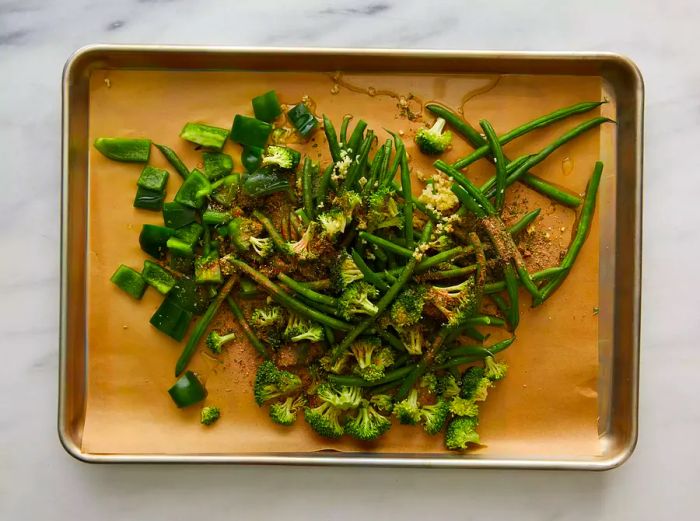 Mixed green veggies and seasonings on a sheet pan