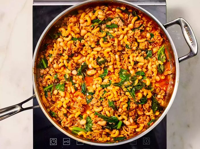 Pasta e Fagioli simmering with added greens and beans in the pan on the stove.