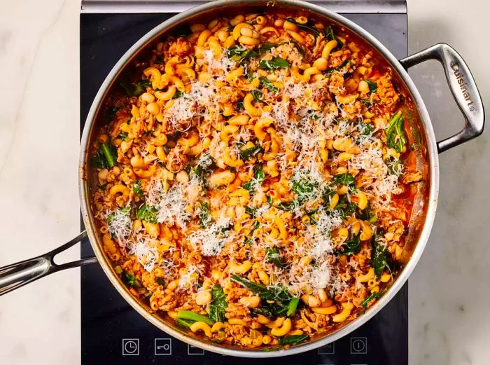 A completed dish of Pasta e Fagioli, topped with grated cheese, resting in a pan on the stovetop.