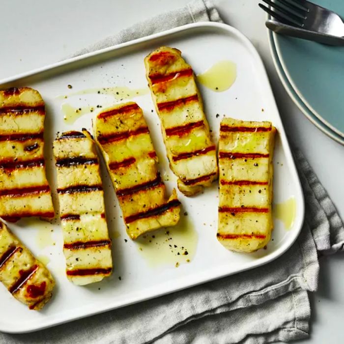 A tray of grilled halloumi drizzled with olive oil and topped with freshly cracked black pepper