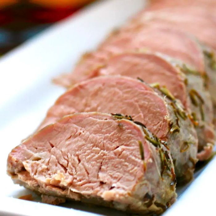 A close-up shot of sliced pork roast served on a white platter.